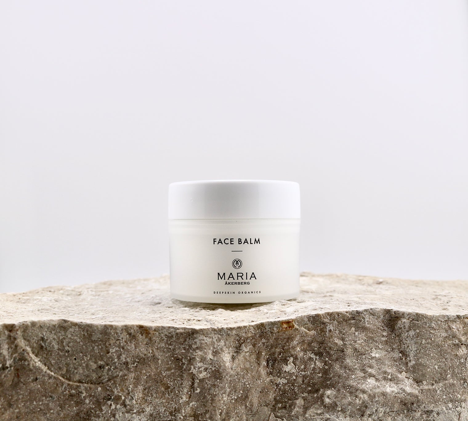 White jar of face balm on a stone surface with a light gray background