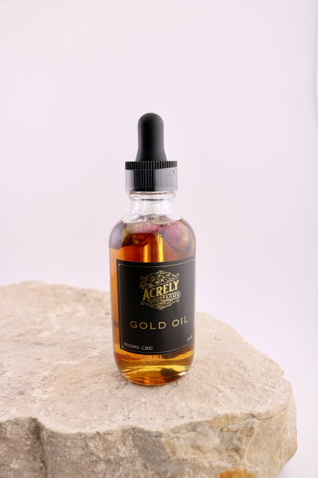 Bottle of Acrely Farms Gold Oil on a stone surface with a white background