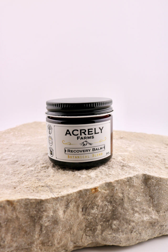 Jar of Acrely Farms Recovery Balm on a stone surface with a white background