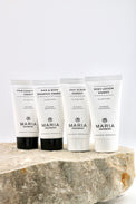 Four white Maria Organics body care tubes standing on a rough stone slab against a clean white background. The tubes are labeled Hair Condition Energy, Hair & Body Shampoo Energy, Salt Scrub Energy, and Body Lotion Energy.