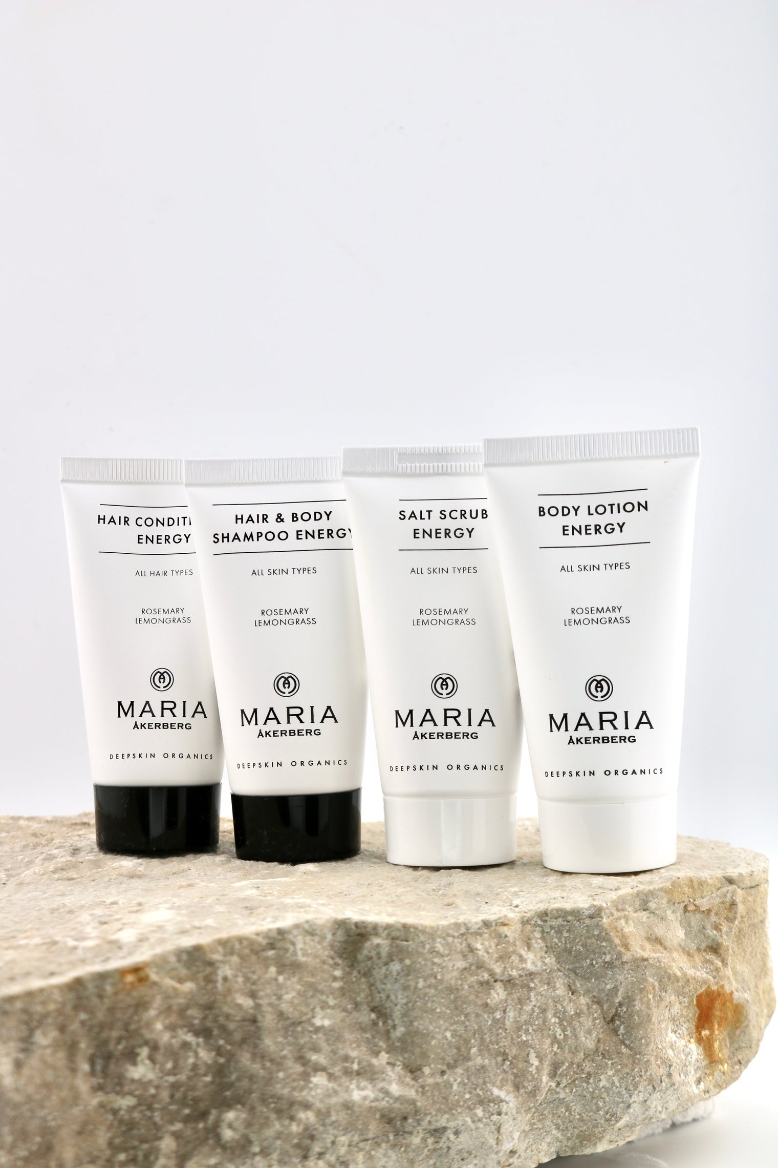 Four white Maria Organics body care tubes standing on a rough stone slab against a clean white background. The tubes are labeled Hair Condition Energy, Hair & Body Shampoo Energy, Salt Scrub Energy, and Body Lotion Energy.