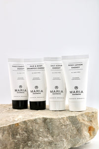 Four white Maria Organics body care tubes standing on a rough stone slab against a clean white background. The tubes are labeled Hair Condition Energy, Hair & Body Shampoo Energy, Salt Scrub Energy, and Body Lotion Energy.