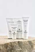 Four white skincare tubes from Maria Akenberg, including Face Lotion Moist, Olive Cleansing, Face Mask Gentle, and Papaya Peeling, arranged on a textured stone surface against a light gray background.