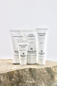 Four white skincare tubes from Maria Akenberg, including Face Lotion Moist, Olive Cleansing, Face Mask Gentle, and Papaya Peeling, arranged on a textured stone surface against a light gray background.
