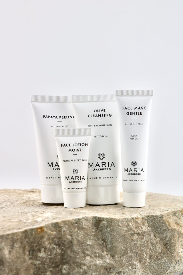 Four white skincare tubes from Maria Akenberg, including Face Lotion Moist, Olive Cleansing, Face Mask Gentle, and Papaya Peeling, arranged on a textured stone surface against a light gray background.