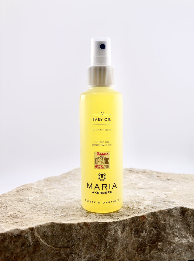 Yellow bottle of Maria Åkersberg baby oil on a stone surface with a white background