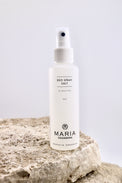 Deodorant spray bottle labeled 'Maria Akerberg' on a rock with a light gray background