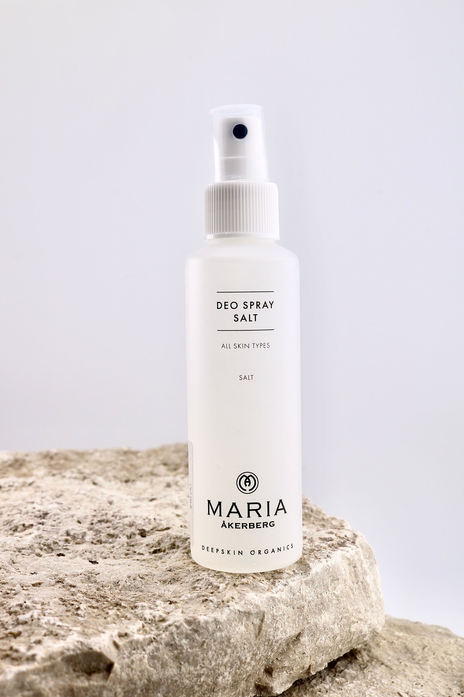 Deodorant spray bottle labeled 'Maria Akerberg' on a rock with a light gray background