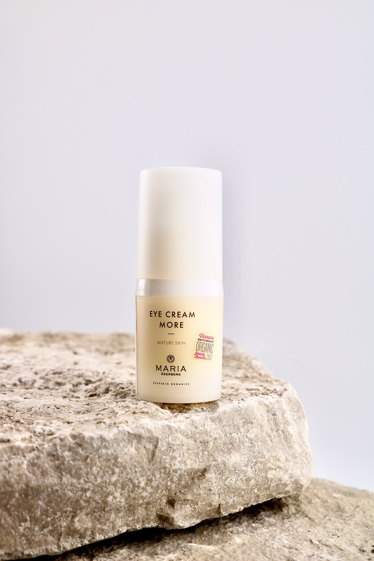 Skincare bottle labeled 'Eye Cream More' by Maria on a stone surface with a light gray background