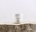 White jar of face balm on a stone surface with a light gray background