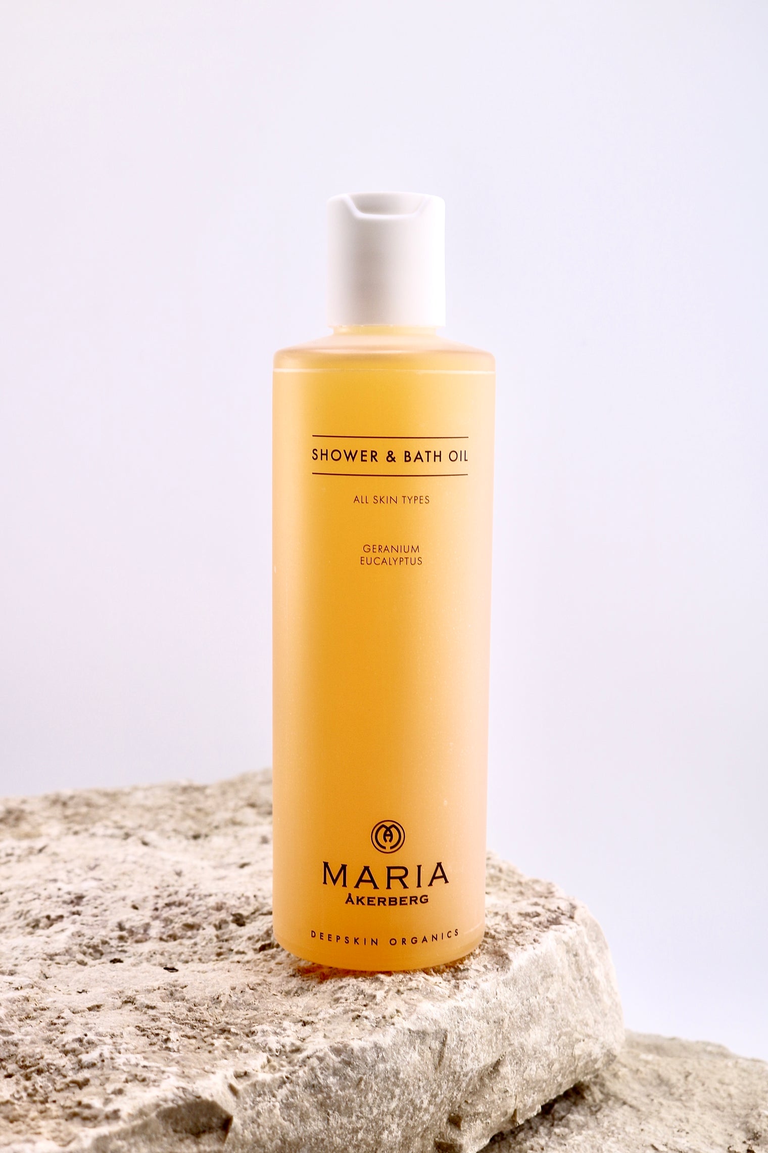 Bottle of Maria Åkerberg shower and bath oil on a textured surface with a light background