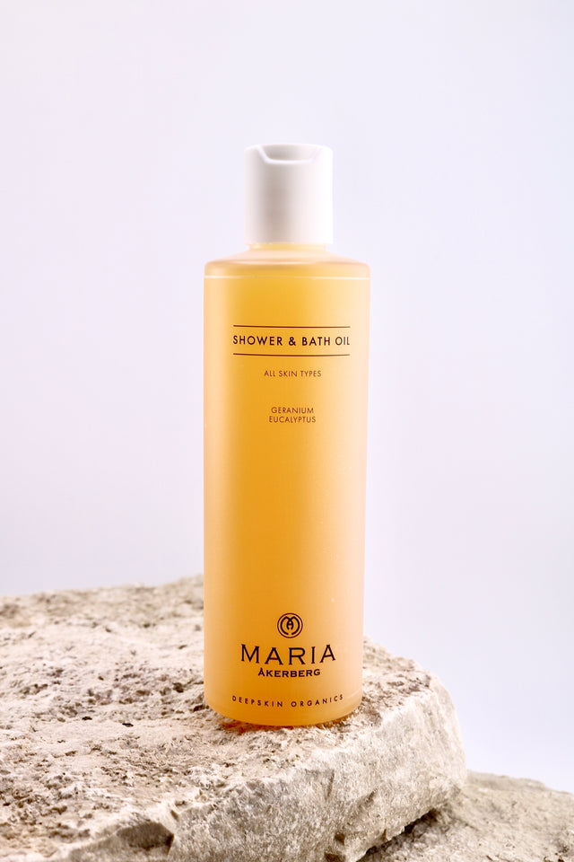 Bottle of Maria Åkerberg shower and bath oil on a textured surface with a light background